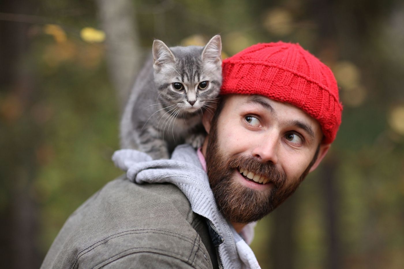 Gato encima del hombro de un joven en la naturaleza
